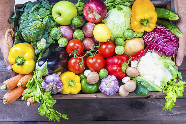 Hands holding fresh veggies in a wooden crate