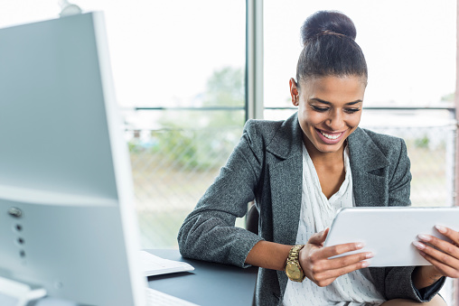 Smiling young woman in office looking on digital tablet