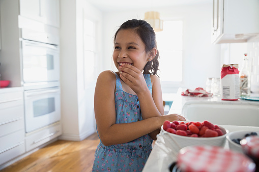 Smiling girl eating fresh berries in kitchen