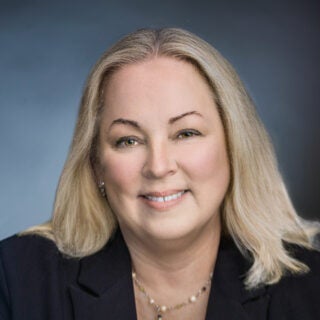 Headshot of Megan Jordan smiling in a dark suit jacket against a gray background.